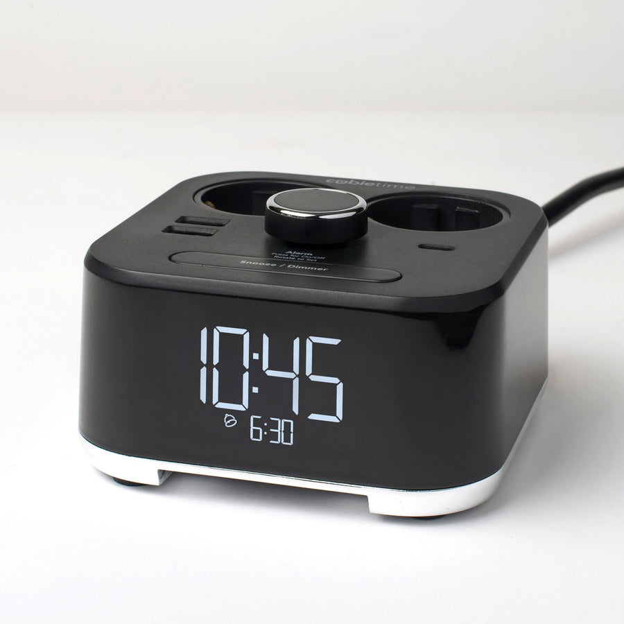 A black digital alarm clock with dual charging ports and a power cord, shown on a clean white background.